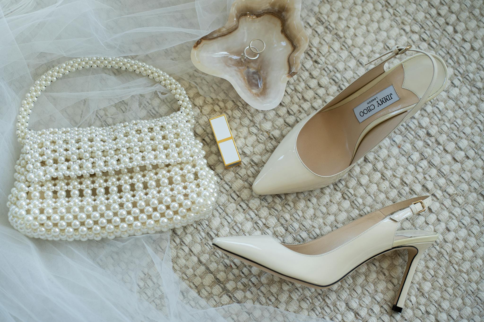 A collection of stylish wedding accessories featuring a pearl handbag, luxury heels, and wedding rings.