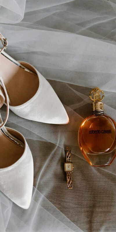 Chic wedding essentials displayed on sheer fabric include white pointed shoes, a stylish watch, and designer perfume.