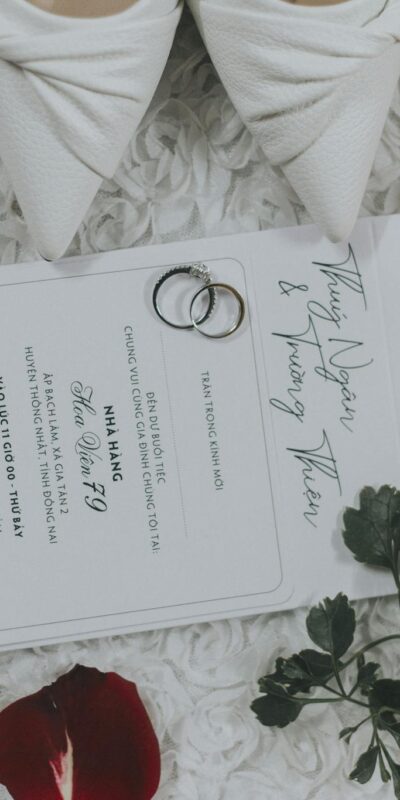 Flat lay of a wedding invitation with rings and perfume, surrounded by petals.