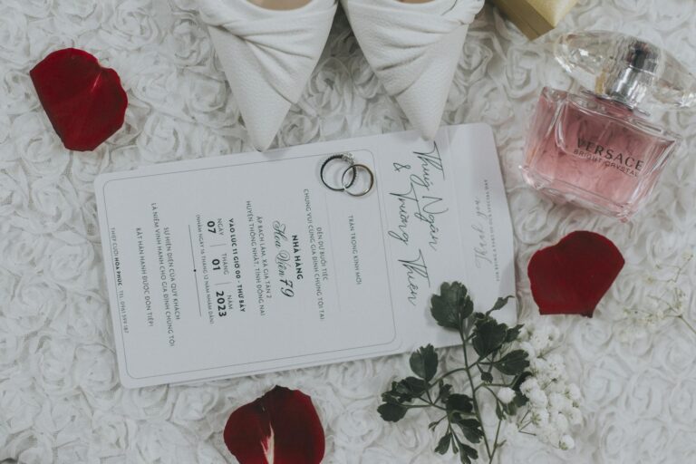 Flat lay of a wedding invitation with rings and perfume, surrounded by petals.
